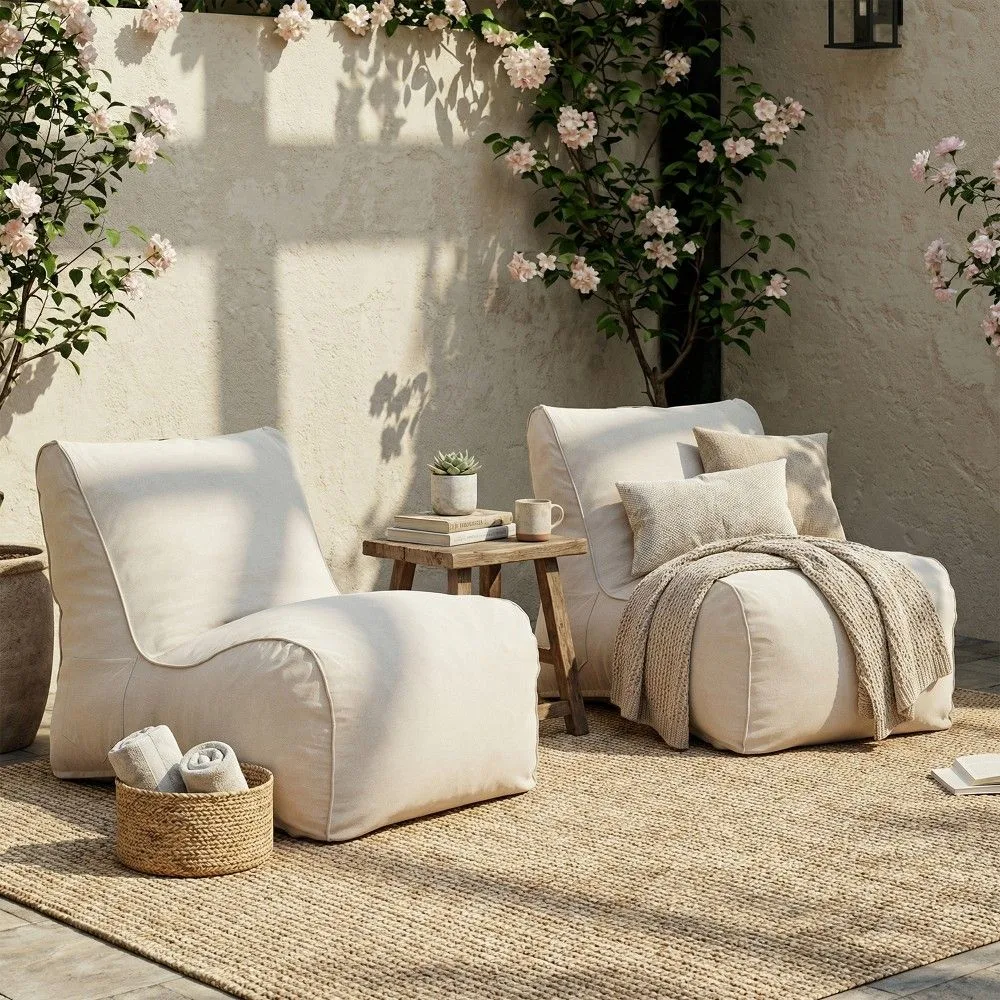 Two cozy cream outdoor lounge chairs placed on a natural jute rug. A simple wooden side table and climbing pink flowers complete this serene and affordable patio design.