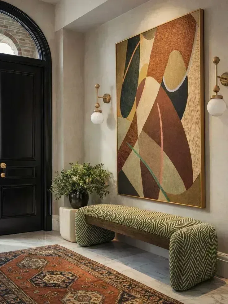 Elegant entryway featuring oversized abstract wall art, a patterned upholstered bench, and brass wall sconces to create a luxurious and curated look, suitable for high-end affordable interior design projects.