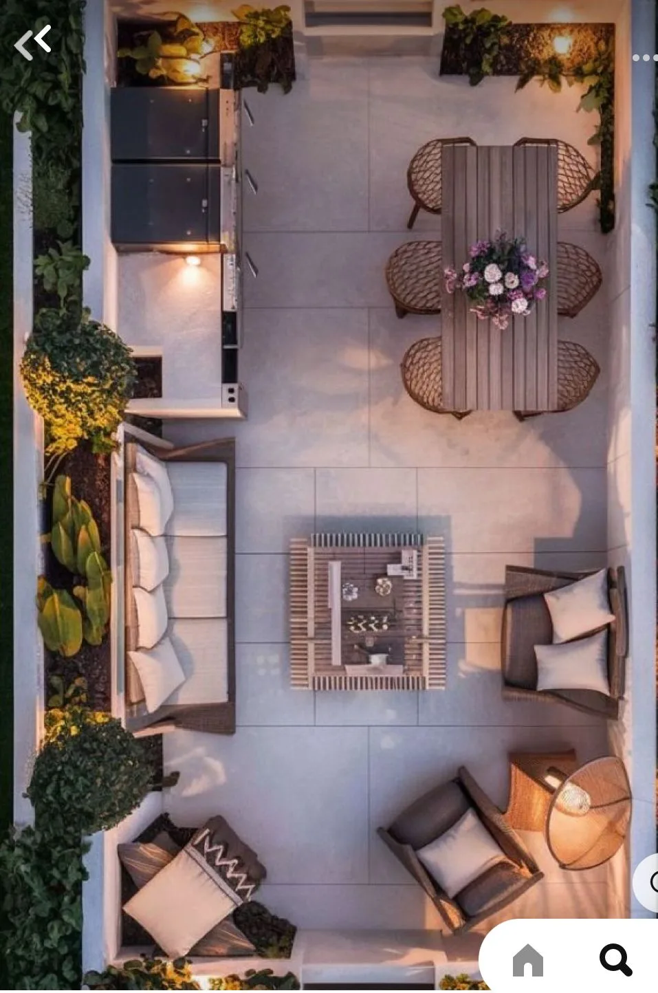 Top-down aerial photograph of a masterfully curated multi-zone outdoor living space. The design, perfect for a modern patio or rooftop terrace, features a fully integrated outdoor kitchen area with a professional grill and integrated lighting at the top-left. Adjacent is a sophisticated outdoor dining area with a large wooden table, matching woven chairs, and a central floral arrangement. A modern slatted coffee table on a large tile surface divides the zones. Below, a generous corner wicker sectional sofa with plush, light-colored cushions and coordinated accent pillows, and an individual accent armchair with a distinct floor-standing lantern, create extensive lounge areas. The space is defined by low white walls, built-in planters with architectural trees, lower-level landscape lighting, and an inviting dusk atmosphere. This showcases a complete, personalized, designer-level layout plan.